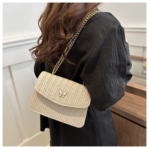 Detail of woven straw crossbody bag featuring a golden chain and white butterfly clasp