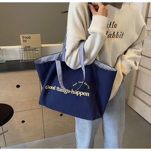 Detailed view of deep blue canvas tote bag with yellow letters on shoulder of a model