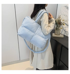 Detail view of the soft light blue quilted puffer shoulder bag worn by a female model