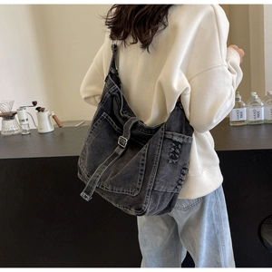 Detail of black washed denim crossbody bag featuring distressed texture and buckle straps