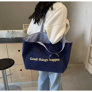 Detail of blue canvas tote bag with 'Good things happen' text and striped lining accents