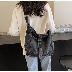 Detail of dark grey washed denim crossbody bag featuring frayed edges and metal buckle