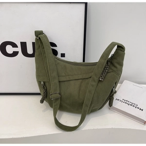 Grass green corduroy crescent crossbody bag with woven knot detail on white table