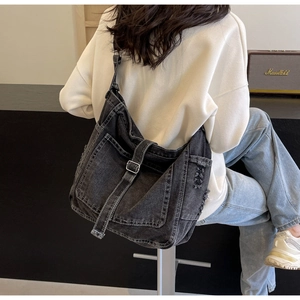 Detailed view of dark grey denim crossbody bag with distressed edges and metal buckles