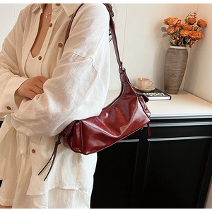 Detail of a dark red minimalist PU leather shoulder bag worn by a model in a cozy room