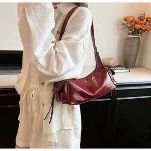Detail view of burgundy glossy shoulder bag with pleated texture and side ribbon tie