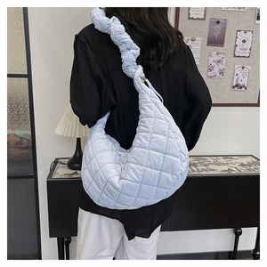 Detail of light blue quilted nylon shoulder bag with stylish ruched strap on model