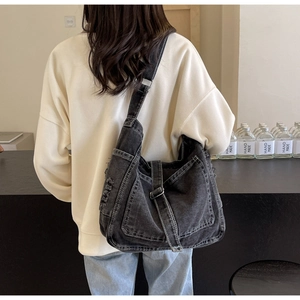 Detail of grey denim crossbody bag with white contrast stitching and adjustable strap