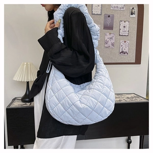 Detailed view of light blue quilted nylon shoulder bag on model in modern room setting
