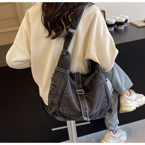 Detail of vintage denim crossbody bag with frayed edges and silver metal buckle adjustment