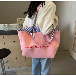 Pink canvas tote bag with Good things happen text and blue striped handles worn by a model