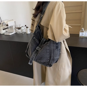 Detail of dark grey denim crossbody bag with frayed edges and buckle closure in a cafe setting