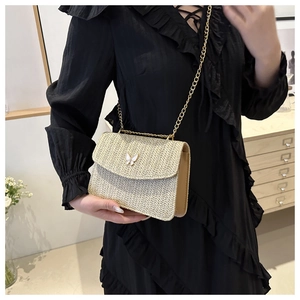 Close-up of woven straw crossbody bag featuring a delicate white butterfly charm and gold chain