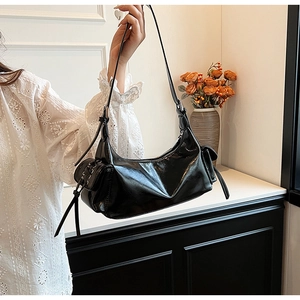 Detail of a black glossy hobo bag with side lace-up pockets and wide shoulder strap