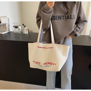 Detailed shot of a cream canvas tote bag with red typography and striped strap lining