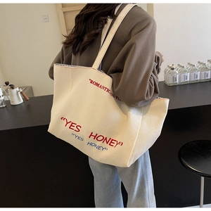 Detail showing high-capacity cream canvas tote bag with vibrant red YES HONEY text print