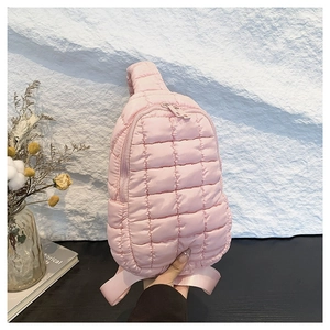 Pink quilted nylon crossbody bag with adjustable strap in a minimalist setting