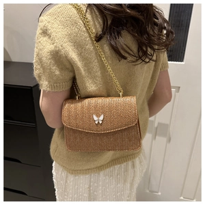 Detail of woven straw crossbody bag featuring a white butterfly clasp and gold chain strap