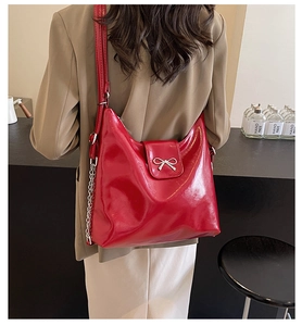 Detail of red patent leather shoulder bag with silver bow buckle worn by a model