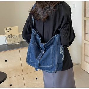 Detail shot of blue denim tote bag with frayed fringe edges and adjustable buckle strap
