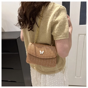 Caramel woven crossbody bag with white butterfly clasp worn by model at back view