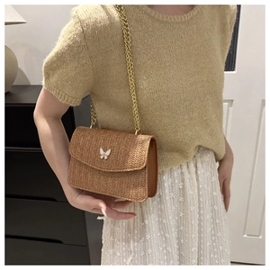 Detail of woven texture shoulder bag with gold chain strap and butterfly metal buckle