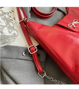 Detail of red faux leather handbag featuring silver metal bow and textured finish