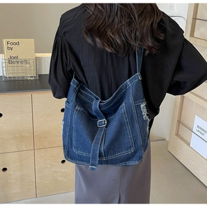 Detail of blue denim crossbody bag with contrast stitching and silver buckle on model