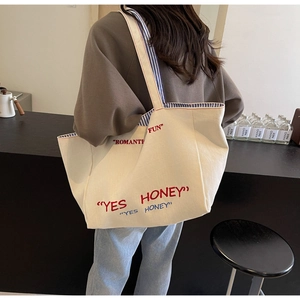 Detail of a beige canvas tote bag with Romantic Fun embroidery and striped inner lining