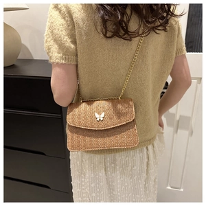 Detail of beige woven crossbody bag with butterfly ornament and gold chain strap on model
