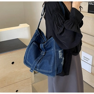 Detail of dark blue denim crossbody bag with contrast stitching and frayed edge design
