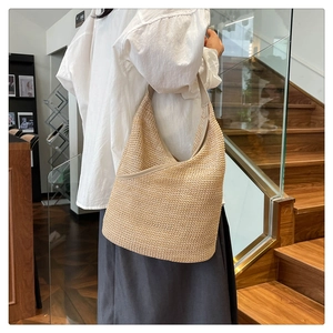 Close-up of beige knitted hobo bag with leather trim and shoulder strap on model