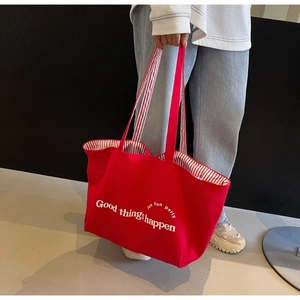 Detail showing the red canvas tote bag with white graphic print and striped handle texture
