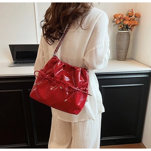Détail du sac seau en cuir verni rouge avec nœud et bandoulière chaîne sur mannequin