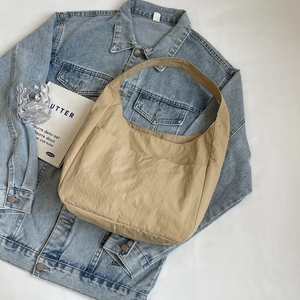 Elegante bolso bandolera media luna beige en nylon sobre fondo vaquero