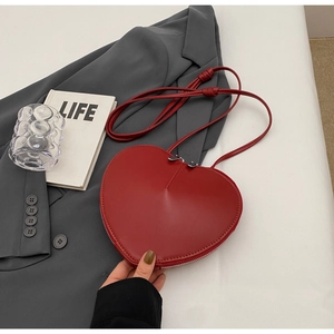 Vista piatta di borsa a tracolla rossa a forma di cuore su tavolo bianco con accessori