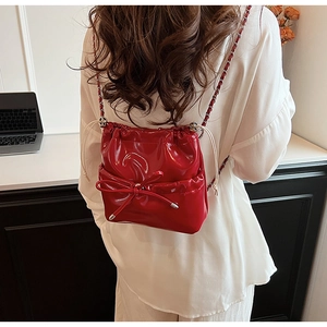 Détail d'un sac seau en cuir verni rouge avec nœud et bandoulière en chaîne argentée