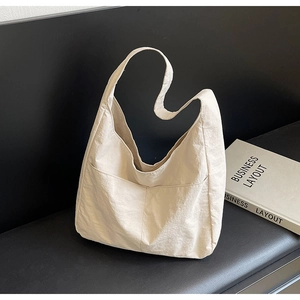 Bolso tote minimalista de nailon beige con bolsillo frontal grande sobre un banco negro