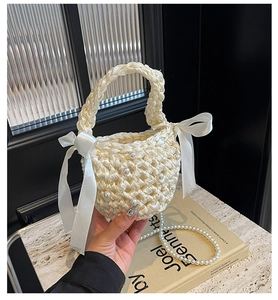 Detail of hand-woven cream fabric bag with pearls, satin bows and pearl chain strap