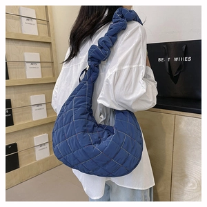 Blue quilted nylon half-moon crossbody bag with ruffled shoulder strap shown on model