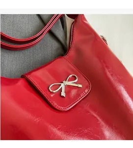 Close-up of a red glossy PU shoulder bag featuring a silver metal bow buckle detail
