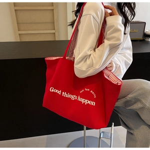 Red canvas tote bag detail showing Good things happen text and striped lining on shoulder