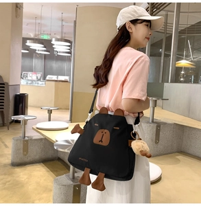 Détail du sac bandoulière en nylon noir avec motif capybara et petit pendentif en peluche