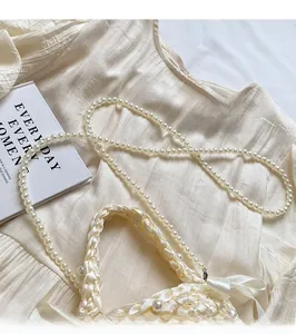 Detail of cream woven handbag featuring pearl shoulder strap and silk bow decoration