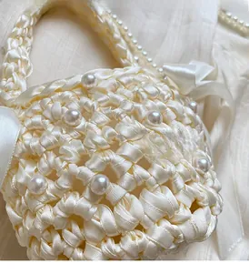 Detailed close-up of woven cream satin fabric with pearl accents and decorative side bow