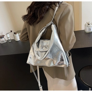 Detail of silver metallic hobo bag featuring chain strap and bow buckle on model