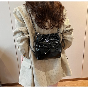 Détail d'un sac seau en cuir PU noir brillant avec nœud décoratif et bandoulière chaîne
