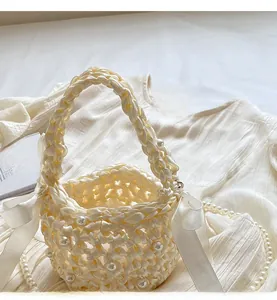 Chic cream woven bucket bag with elegant pearl accents and decorative silk ribbons