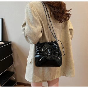 Détail d'un sac seau noir brillant avec nœud papillon et bandoulière en chaîne métal