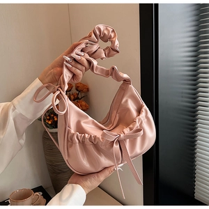 Detail of light pink PU leather crescent bag featuring a bow and pleated handle